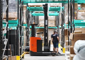 Warehouse scene featuring workers and a forklift navigating aisles for logistics and inventory management.