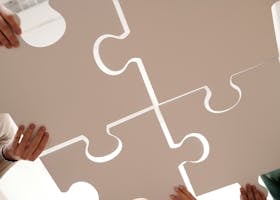 Hands of diverse individuals holding large puzzle pieces, symbolizing teamwork and unity.