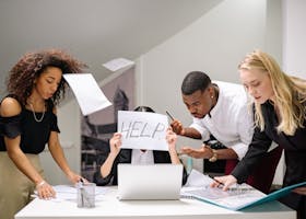 Team of stressed colleagues in an office dealing with paperwork chaos, asking for help.