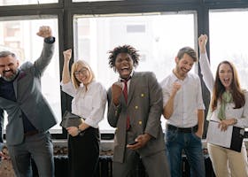 A joyful, diverse group of colleagues celebrating success indoors with cheerful expressions.