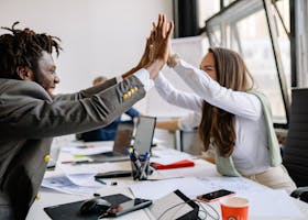 Multiracial colleagues celebrating a successful meeting with a high five in a modern office setting.