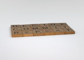 Wooden tiles arranged to spell 'DECIDE COMMIT REPEAT' on a white background.